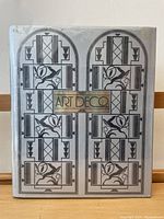 Front cover of the book showing Art Deco dust jacket design with geometric and floral patterns in black and silver, title in gold rectangle