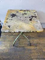 Front view of the weathered folding table showing the square table top with peeling paint and patina.