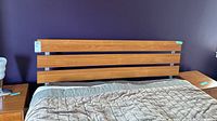 Queen size wooden headboard photographed upright against a purple wall, showing three horizontal wooden slats and metal connectors on sides.