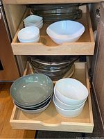 Drawers filled with white and grey ceramic bowls, some are ribbed. Wooden salad bowl also visible. Chips noted on items.