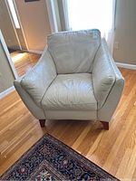 Front view of light-colored leather armchair on wooden floor with rug nearby, showing cushioned seat and backrest.