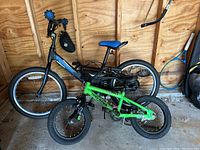 Two children's bikes in a garage, one black and blue, one green Tony Hawk Climber.
