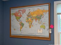 Full view of rectangular cork board with world map pinned on it, mounted on wall.