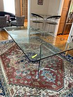 Front angled view showing the top surface and curved base of the glass dining table on a patterned rug.