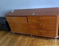 Front view of 6-drawer wooden dresser with silver knobs, showing scratches and wear on surface.