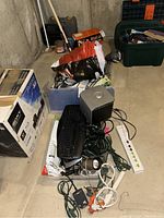 View of the lot placed on a concrete floor showing extension cords, surge protector, black keyboard, Dell speaker, various cables, and a desk lamp.
