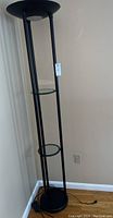 Full view of one black floor lamp showing its three round glass shelves and slim design, with black metal supports and round base