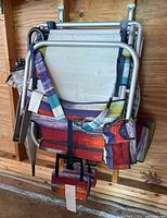 Two folded Tommy Bahama folding beach chairs with colorful striped fabric and aluminum frames hanging on wall, clear vinyl umbrella hanging with them