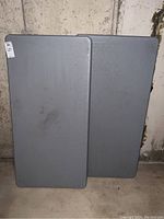 Two gray folding tables stacked, showing their rectangular plastic tops with some marks and wear.