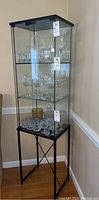 Full view of the tall glass display cabinet with glass shelves holding various types of glassware including wine glasses and tumblers.