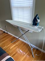 Full view of ironing board set up near window, showing striped cover and iron placed on board.
