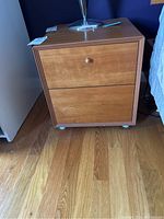 Front view of one nightstand showing two drawers, wood grain finish, with one drawer missing a handle.