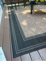 Close-up of rug corner showing woven texture with beige center and black border with gray stripes.