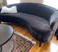 Angled front view showing curved shape, upholstery color, pillow placement and wooden legs.