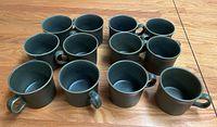 Set of 12 green ceramic mugs displayed together on table to show quantity and condition.