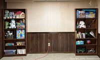 Two bookshelves shown against a wall, empty except for toys and books (not included in sale).