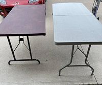 Full front view of 5ft wooden table and 6ft folding plastic table on concrete driveway beside a red car.