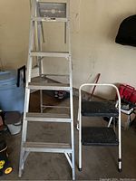 6-foot aluminum step ladder and small two-step stool in garage, showing both items and surroundings.
