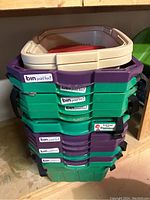 Stack of 14 plastic bins with black straps and 'bin paid for!' stickers