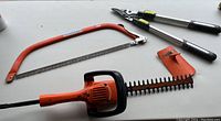 Photo showing the full lot including the hedge trimmer, hand saw, and tree lopper on a white surface.