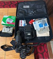 Full layout showing Fujifilm camera with boxed packaging, Minolta X-700 camera with Makinon lens, Blacks flash, accessories, and carrying case