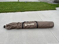 Closed shelter packed inside brown carrying bag with Clam logo, laid flat on concrete.