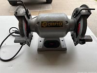 Front view of Craftex bench grinder showing the two grinding wheels, power cord, tool rests, and brand label.