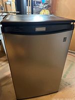 Full view of the Danby mini fridge showing black top and silver door panel with handle on top part.
