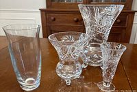 Four crystal vases on wooden table with a cabinet in background. Includes one large cut Bohemia crystal vase and three smaller cut pinwheel crystal vases.