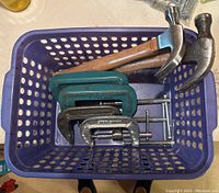 Top view of the basket containing two claw hammers with wooden handles and four adjustable C-clamps.