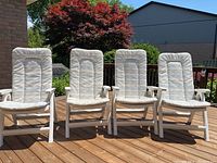 Four white plastic high back lawn chairs with cushions on wood deck