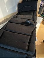 Full view of the black body massage pad showing padded segments and some pet hair on surface.