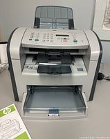 Front view of HP LaserJet M1319f MFP laser printer showing keypad, LCD screen, and paper trays.