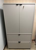Front view of gray metal office cabinet with two lower drawers and lockable double upper doors.