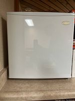 Closed view of white Salton mini fridge unit on a countertop.