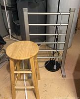 Photo showing free standing towel warmer behind wooden stool and black floor lamp in basement setting