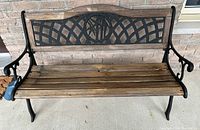 Front view of wooden bench with black wrought iron lattice backrest, wooden slats seat, and curved armrests.