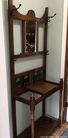 Front view of the antique wooden hall tree showing mirror, hooks, green tile back panel, and wooden seat
