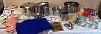 Wide view showing the full assortment including pots, pans, mixing bowls, cookie cutters, linens, and egg beater.