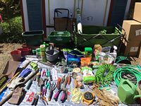 Full overview of the gardening supplies lot showing tools, hoses, gloves, watering cans, and plant food.