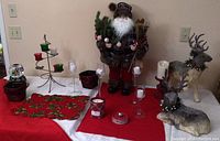 Wide view of Christmas decor items displayed on white and red linens including large Santa figurine, reindeer, candle holders, and snow globe.