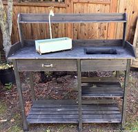 Full front view of black painted wood garden potting table with drawer and shelves, showing integrated sink and metal pot on top
