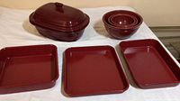 Full view of three red metal baking pans, set of three red nesting mixing bowls, and one red covered ceramic baking dish.