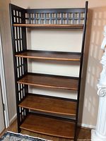 Front view of black framed shelf with 5 brown shelves against a wall, showing lattice side and back design