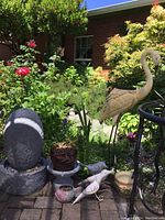 Wide shot showing the full assortment of yard art and garden items including birds, fountain, and planters in a garden setting.