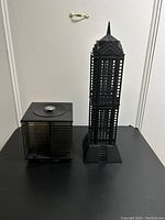 Two black plastic CD holders: a tall tower-shaped perforated holder with pointed top and a smaller cube-shaped rotatable holder.