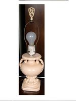 Front view of vintage beige ceramic table lamp without shade, showing detailed sculpting and metal harp with finial.