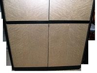 Front view of the cabinet showing four textured gold laminate doors with black horizontal handle trim at center and solid black base.