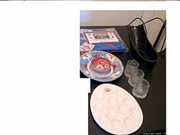 Image showing a sealed poker tablecloth, decorative plate and bowl with colorful patterns, three small clear glasses, a white oval seafood platter, and a black metal tray.