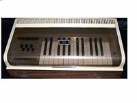 Magnus chord organ with a transparent hinged cover, keyboard and four black knobs, showing front top view.